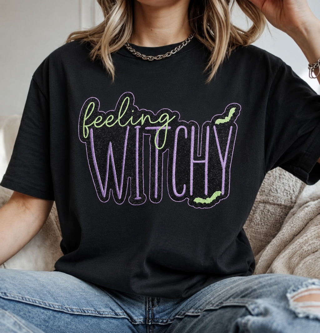 Untapped Innovations black crewneck t-shirt with Feeling Witchy glitter graphic, purple and neon green bat accents.