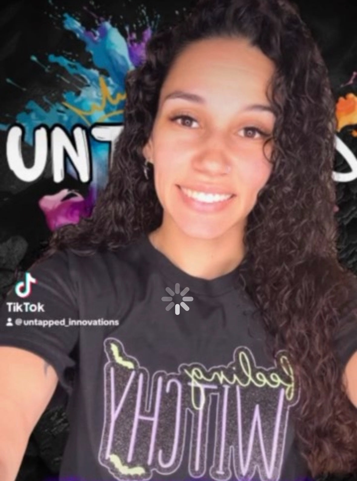 Untapped Innovations black crewneck t-shirt with Feeling Witchy glitter graphic, worn by a woman with curly hair.