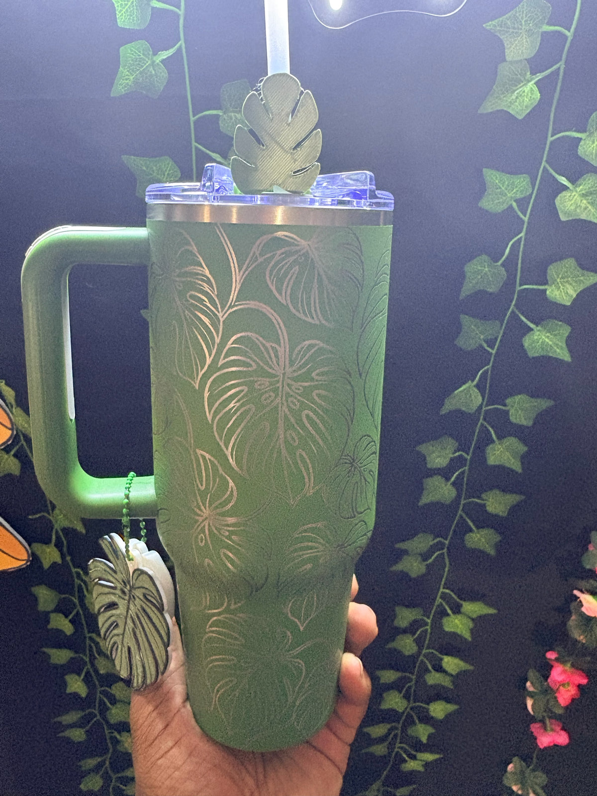 Untapped Innovations green stainless steel insulated tumbler with etched monstera leaf pattern, handle, and leaf charm.