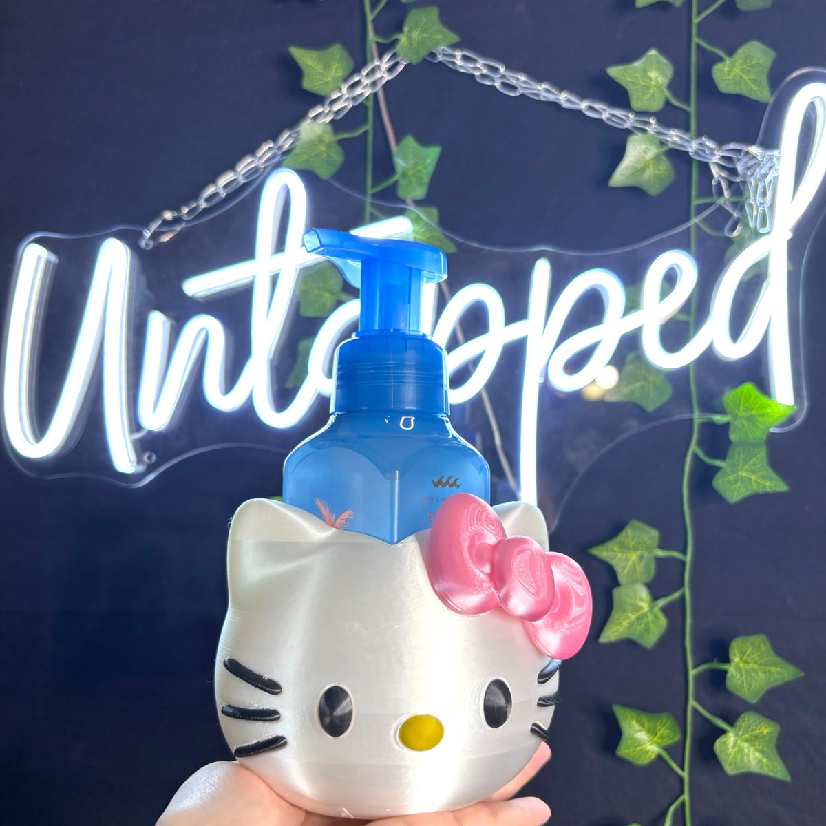 Untapped Innovations Hello Kitty character soap dispenser holder with a blue foaming soap bottle on a dark background
