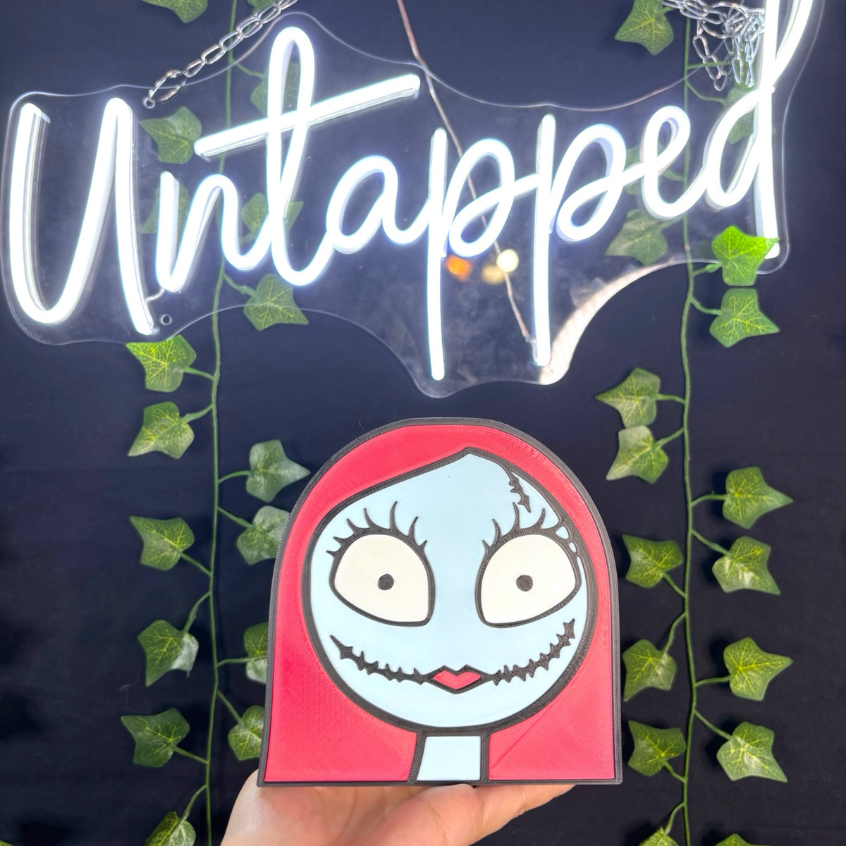 Untapped Innovations Sally ragdoll wall plaque with red hair and stitched face on a black background with ivy